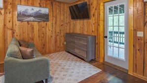 Une pièce aux murs en bois, avec un canapé vert doté de coussins marron, un téléviseur à écran plat, un meuble en bois et une porte donnant sur l’extérieur.