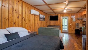 A wooden-paneled room with a bed, a sofa, a television, and a door leading outside. - Cozy, Modern Black Cabin Retreat - Mins. to Cloudland Canyon & Lookout Mountain (Rising Fawn)