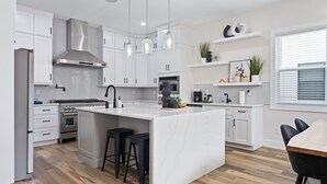 Een moderne keuken met witte kasten, een centraal eiland met krukken, roestvrijstalen apparatuur en hanglampen.