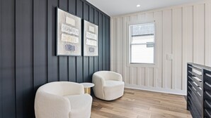 Een moderne kamer met twee witte fauteuils, een klein rond tafeltje en een groot raam met jaloezieën.