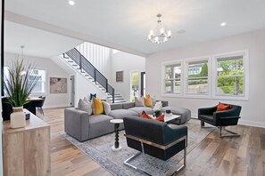 A spacious living room with a grey sectional sofa, a dark armchair, and a coffee table. A staircase with black railings leads to an upper level. - Cozy, Modern Retreat in the Heart of College Park Perfect for Families & Guests! (College Park)