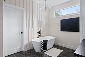 Une salle de bain moderne avec une baignoire sur pieds, une porte blanche, une serviette à motifs noirs et blancs, une œuvre d’art noire accrochée au mur et un sol à motifs.