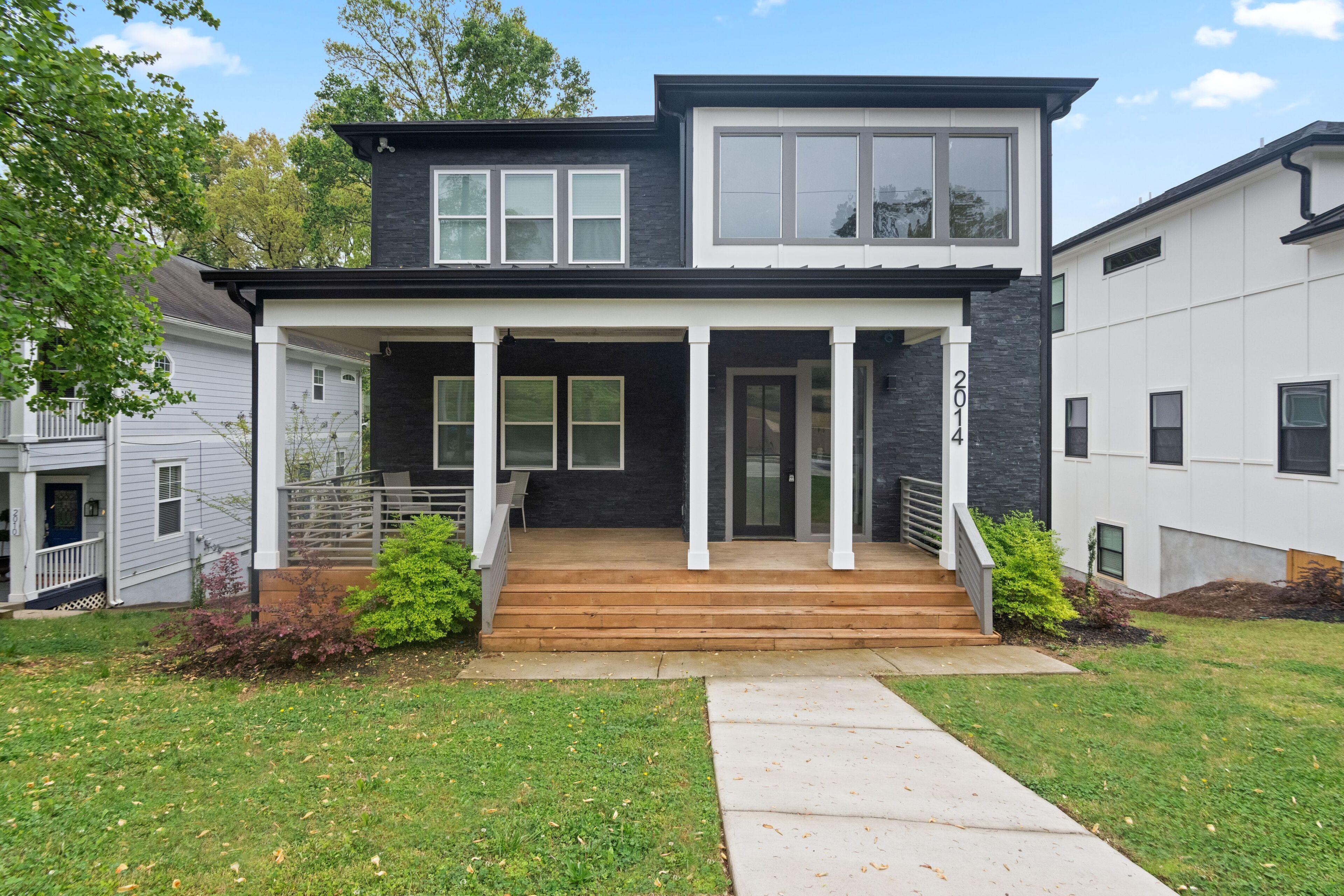 A modern two-story house with a front porch, a staircase leading to the entrance, and a well-maintained lawn.