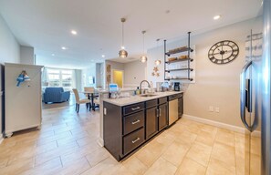 A modern kitchen with a central island, stainless steel appliances, pendant lighting, and a wall-mounted clock. - Downtown 2BR Condo Near Beach & Boardwalk (Ocean City)