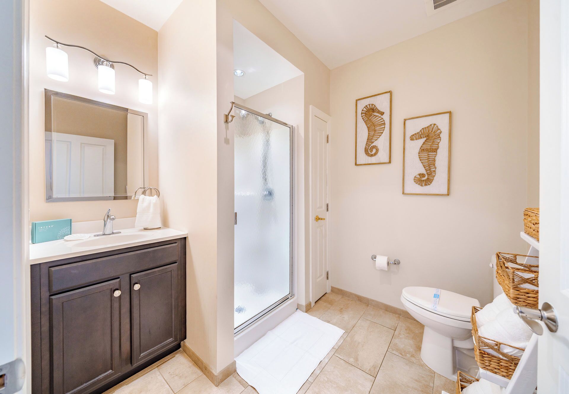 Een badkamer met een donker houten wastafelmeubel, een douchecabine van glas, een toilet en twee afbeeldingen van zeepaardjes in lijsten aan de muur.