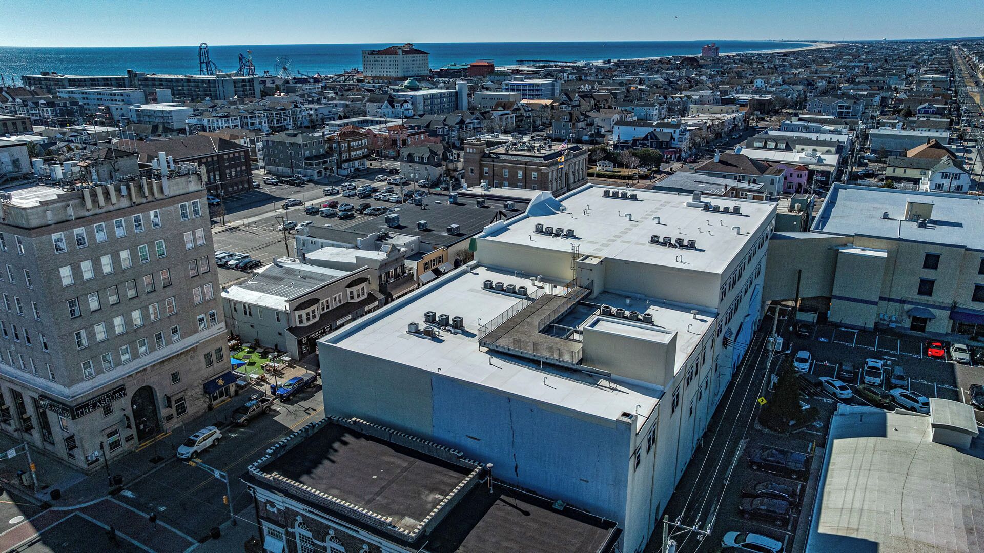 A coastal cityscape with a mix of residential and commercial buildings, including a prominent hotel with a flat roof and multiple air conditioning units.