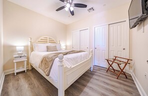 Une chambre à coucher avec un lit, des tables de chevet, un ventilateur de plafond et une chaise en bois.