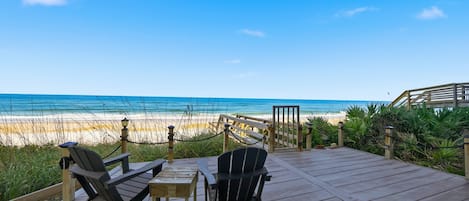 Une terrasse en bois avec deux fauteuils Adirondack et une petite table, le tout donnant sur une plage.