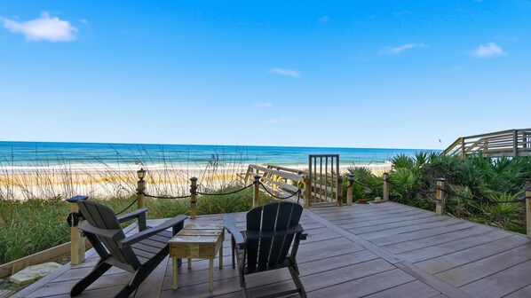 Terraza de madera con dos sillas Adirondack y una mesita pequeña con vistas a la playa.