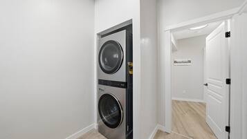 Un cuarto de lavandería con dos lavadoras apiladas y una puerta que da a otra habitación.