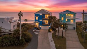 Une maison à deux étages avec un balcon, une allée et une vue sur l’océan au coucher du soleil.
