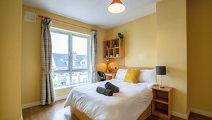 A hotel room with a large bed, a bedside table with a lamp, a small desk with a chair, a window with curtains, and a shelf with plants. - 106 -The Townhouse by Shortstays (Galway)