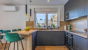 Een moderne keuken met een centraal eiland, donkere keukenkastjes en een raam met uitzicht op bomen.
