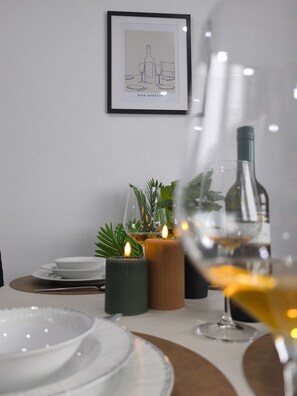 Un tavolo da pranzo con piatti bianchi, bicchieri e una candela. Al di sopra del tavolo, un quadro appeso al muro.