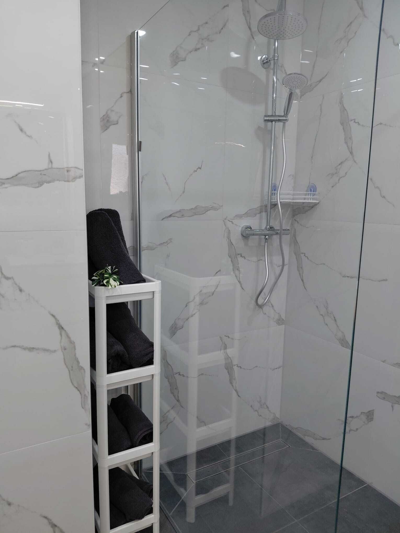 Ein modernes Badezimmer mit Duschkabine aus Glas, einer weißen Marmor-Spritzschutzwand und einem Handtuchhalter mit gefalteten Handtüchern.