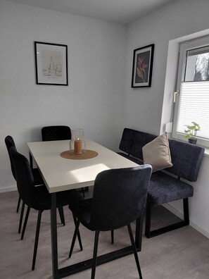 Un espace repas moderne avec une table blanche, des chaises noires et un canapé bleu. Deux œuvres d’art encadrées ornent les murs.
