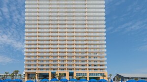 Ett högt hotell med flera balkonger, en central entré och en klar himmel.