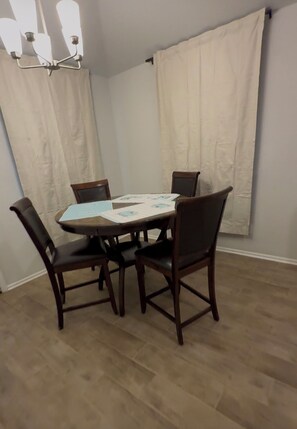 A dining area with a table, four chairs, a chandelier, and curtains.