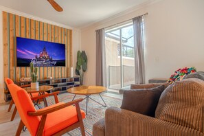 A living room with a flat-screen TV, orange chairs, a brown sofa, and a large window. - Spacious 4BR Townhome w/ Private Pool • Storey Lake Resort • Near Disney (Kissimmee)