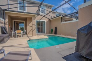 A backyard with a swimming pool, a covered patio, and a door leading to a covered area. - Spacious 4BR Townhome w/ Private Pool • Storey Lake Resort • Near Disney (Kissimmee)