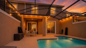 A backyard with a swimming pool, a covered patio, and string lights. - Spacious 4BR Townhome w/ Private Pool • Storey Lake Resort • Near Disney (Kissimmee)