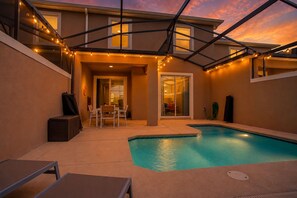 A backyard with a swimming pool, a covered patio, and string lights. - Spacious 4BR Townhome w/ Private Pool • Storey Lake Resort • Near Disney (Kissimmee)