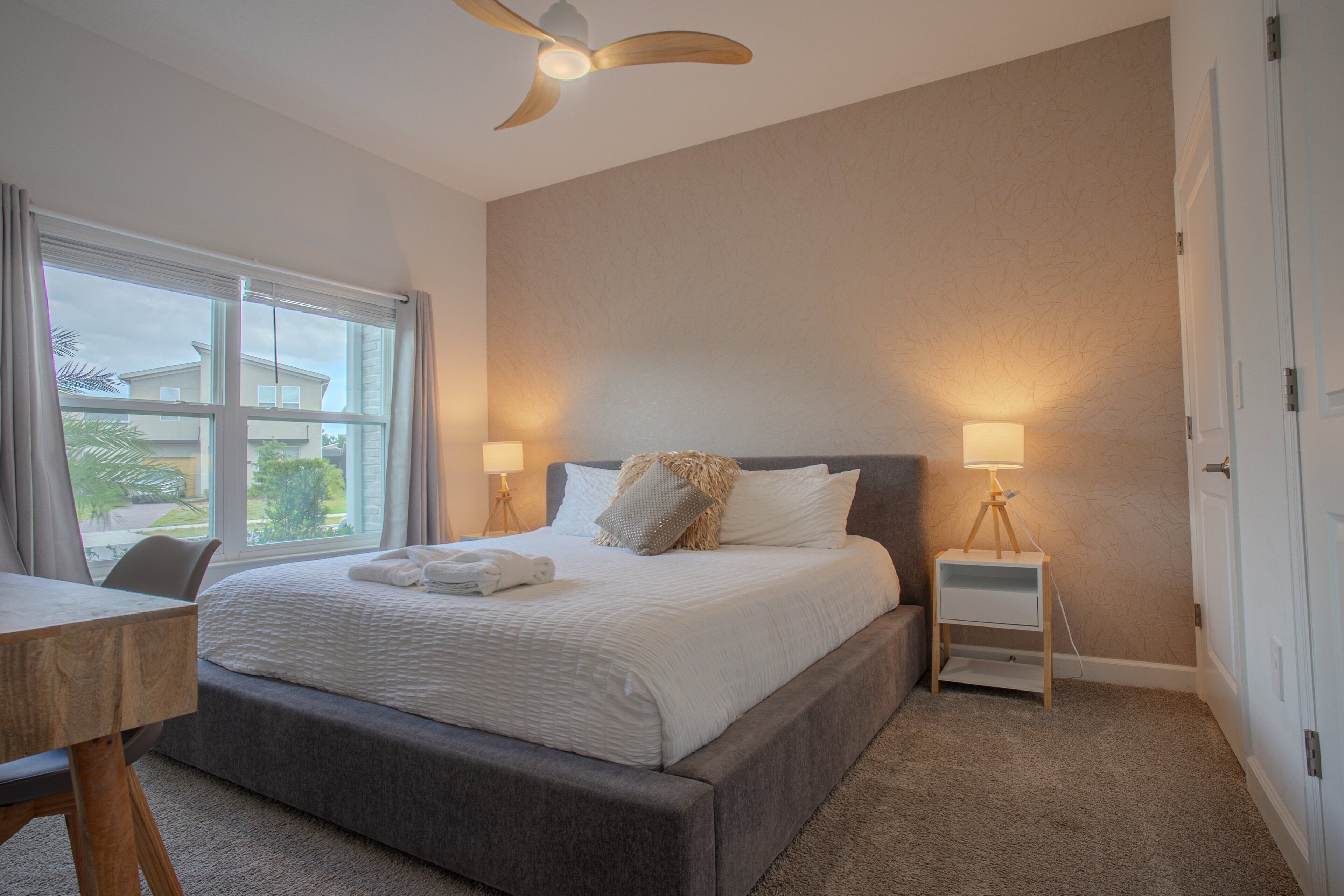 Een slaapkamer met een bed, nachtkastjes, een plafondventilator en een raam.