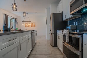 A modern kitchen with stainless steel appliances, a central island, pendant lighting, and a view into the dining area. - Spacious 4BR Townhome w/ Private Pool • Storey Lake Resort • Near Disney (Kissimmee)