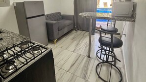 A compact kitchen with a gas stove, a refrigerator, a sofa, and a small dining area with a table and two chairs. - Studio Au Centre-ville à 2 Minutes de la Plage 105 (Sosúa)