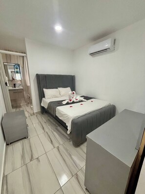Ein Hotelzimmer mit einem Bett, einem kleinen Schreibtisch, einem Koffer und einer Klimaanlage.