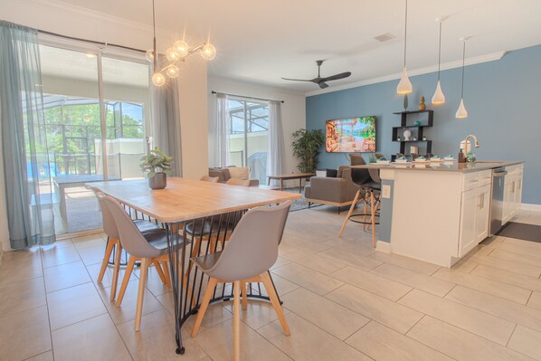 A modern kitchen with a central island, dining area with chairs, and a large window with curtains. - Family-Friendly 4BR Townhouse with Private Pool at Storey Lake Resort – Near Disney (Kissimmee)