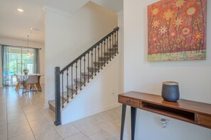 A staircase with a wooden handrail and carpeted steps, a dining area with a table and chairs, and a painting of flowers on the wall. - Family-Friendly 4BR Townhouse with Private Pool at Storey Lake Resort – Near Disney (Kissimmee)