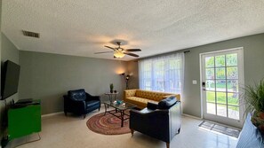 A living room with a ceiling fan, a sofa, a chair, a television, and a window with a view of greenery. - Sunny Siesta Key Retreat w/ Private Heated Pool | 2BR | Dog-Friendly (Siesta Key)