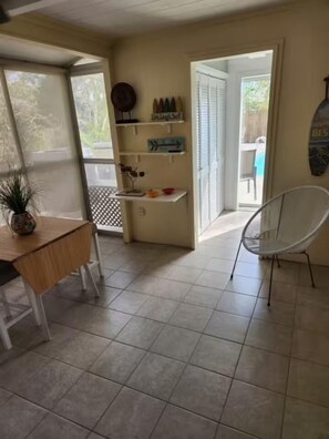 A room with a wooden table, a white chair, a small shelf with decorative items, and a view of the outdoors through a door. - Sunny Siesta Key Retreat w/ Private Heated Pool | 2BR | Dog-Friendly (Siesta Key)