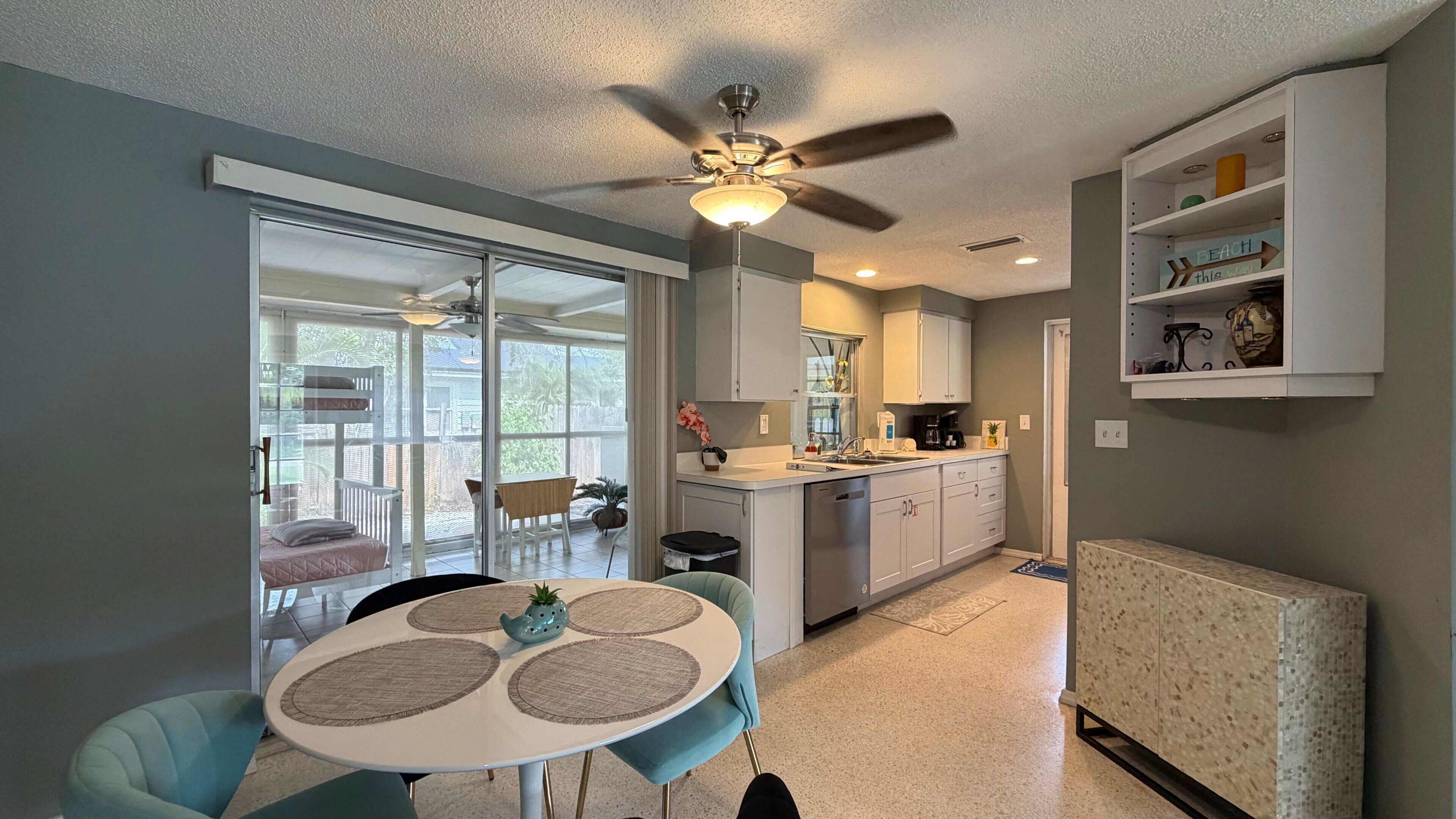 A modern kitchen with a built-in oven, a dining area with a round table and chairs, and a ceiling fan.