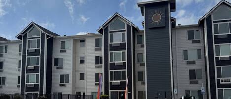 A multi-story building with a central tower, a parking lot, and a clear sky.