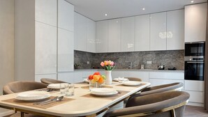 Una cocina moderna con armarios blancos, salpicadero de mármol y horno Bosch.