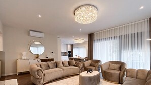 Una sala moderna con un sofá curvo, un otoman redondo y un sillón circular. Se aprecia un comedor al fondo con una mesa y sillas.