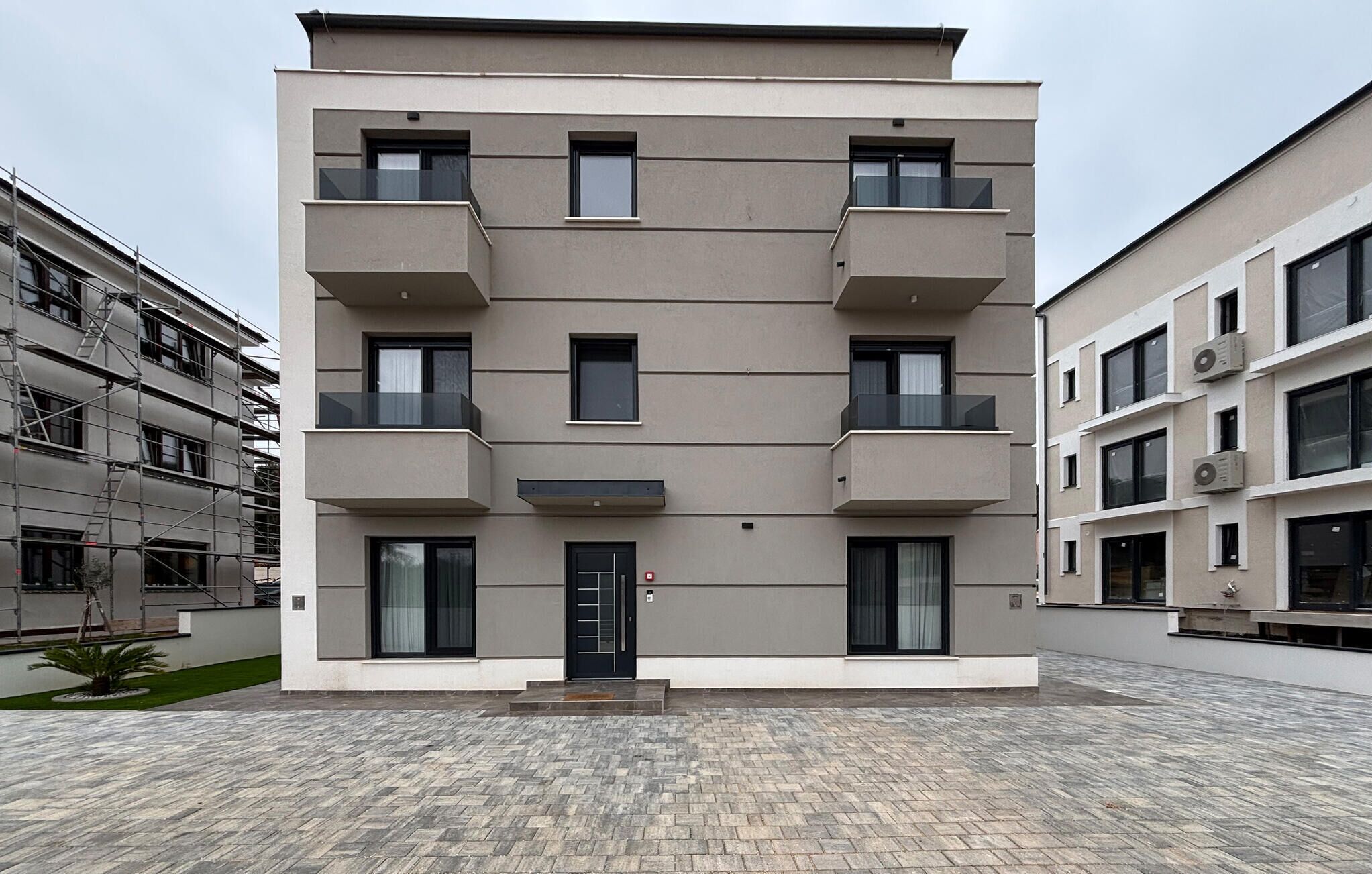 A multi-story residential building with balconies, a central entrance, and a paved courtyard.