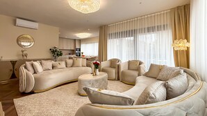 A luxurious living room with a large L-shaped sofa, a round coffee table, and two armchairs. There is a chandelier hanging from the ceiling, and a kitchen is visible in the background. - Cozy apartment in Rovinj with house sea view (Rovinj)