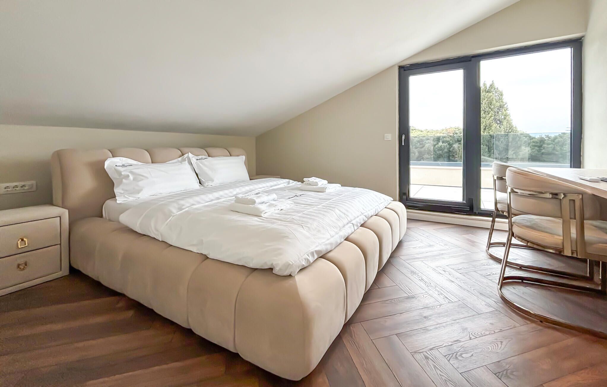 A bedroom with a large bed, a desk, and a view of the outdoors through a sliding door.