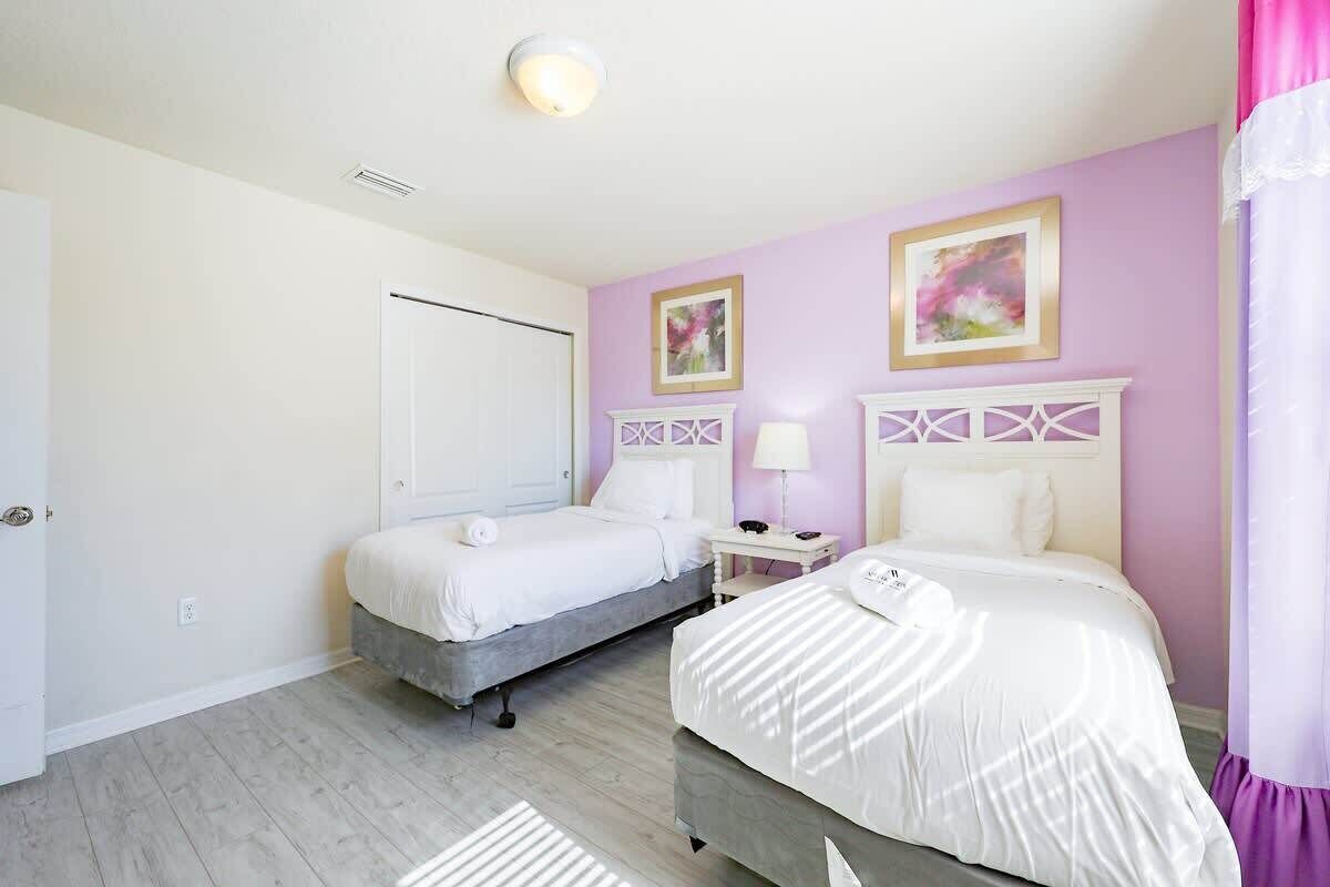 A bedroom with two beds, a white door, and a ceiling light.