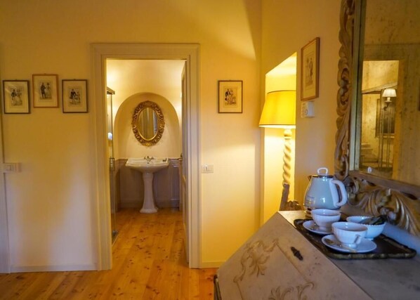 A hotel room with a wooden floor, a sitting area with a table set for tea, a mirror, and framed pictures on the walls. - Villa Dorigny Dimora Storica (Verona)