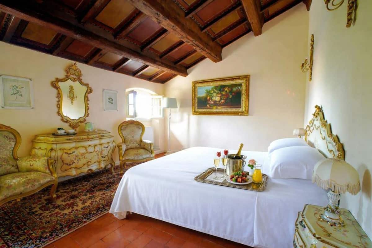 A room with a bed, a chaise lounge, a dresser, and a painting on the wall.