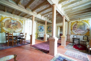 A room with ornate ceiling frescoes, large columns, and a dining area with chairs and a table. - Villa Dorigny Dimora Storica (Verona)