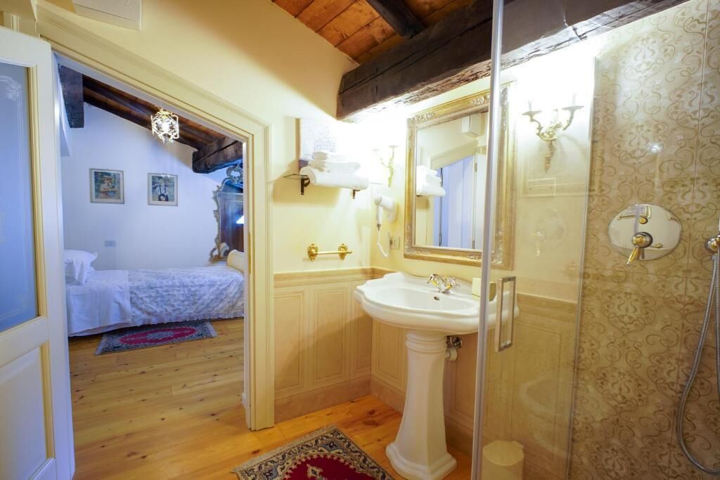A bathroom with a pedestal sink, a glass shower enclosure, and a wooden floor.