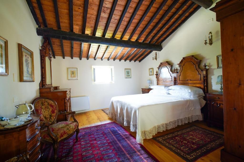 A bedroom with a wooden ceiling, a bed with white linens, a wooden dresser, a chair, and a patterned rug.