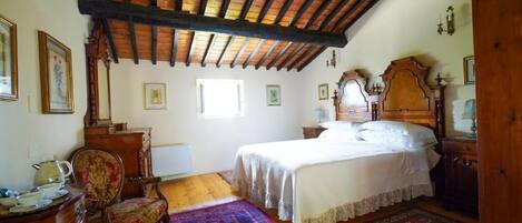 A bedroom with a wooden ceiling, a bed with white linens, a wooden dresser, a chair, and a patterned rug.