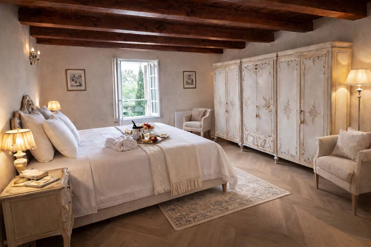 A bedroom with a large bed, a wardrobe, a chair, and a nightstand with a lamp.