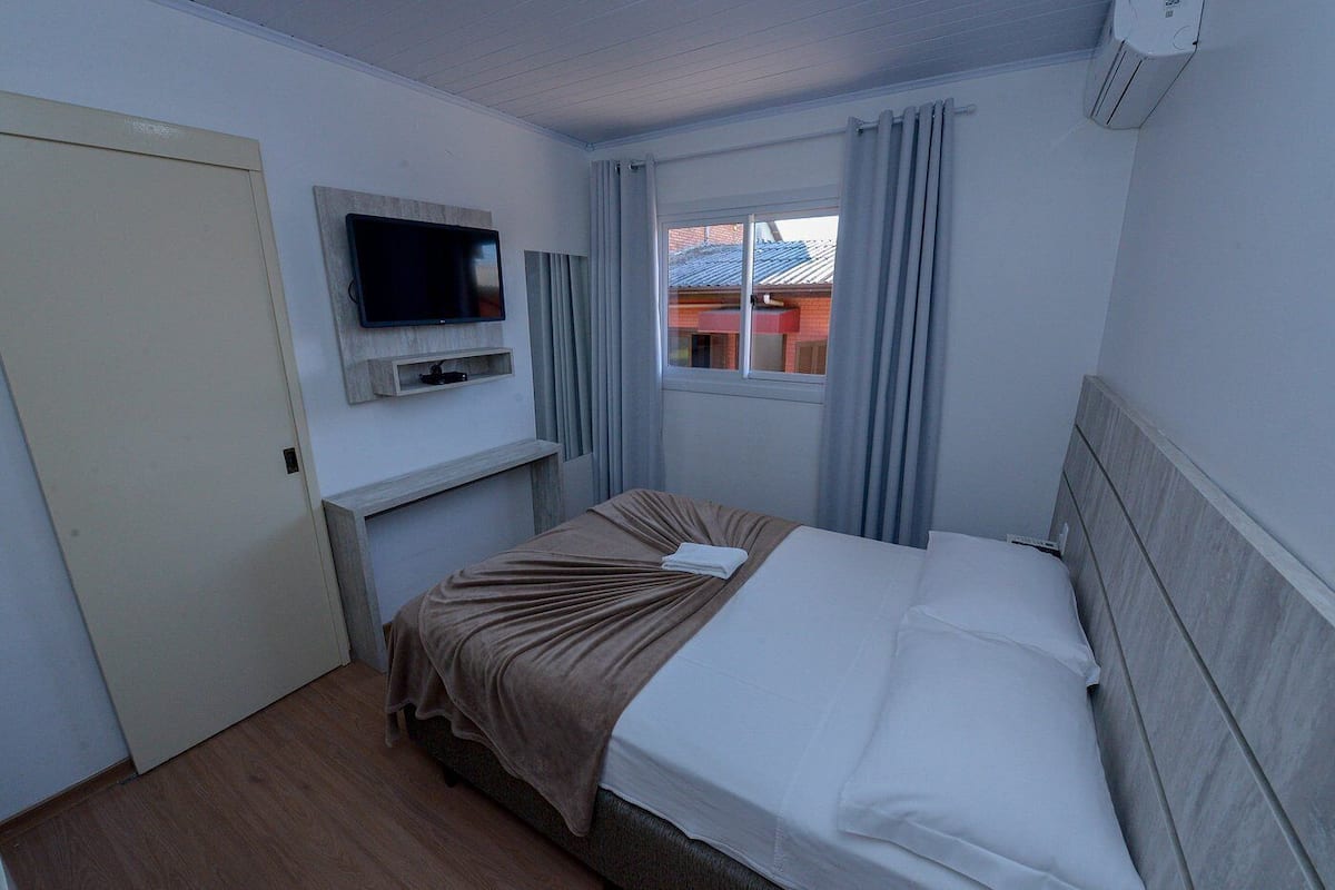 A hotel room with a bed, a television mounted on the wall, a window with curtains, and a door.